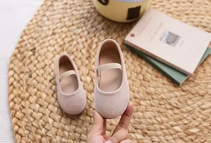 Detail of pink suede Mary Jane kids shoes with elastic strap on a woven mat background