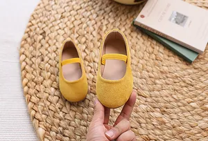 Detail of yellow suede Mary Jane flat for girls with elastic strap on woven mat