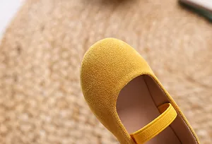 Detail of yellow fabric Mary Jane kids shoes with elastic strap on a textured mat
