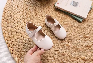 Nahaufnahme beiger Mary Jane Kinderschuhe mit Wellenrand und Klettverschluss auf Stroh