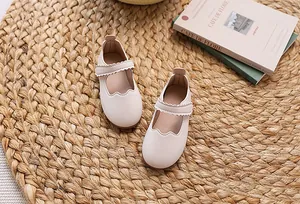 Details beige Mary Jane Kinderschuhe mit Wellenrand auf einer gewebten Matte mit Büchern