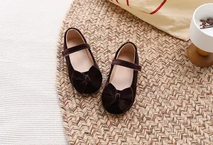 Detailopname van donkere fluwelen Mary Janes voor meisjes met een strik op een mat