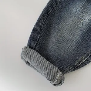 Detail of distressed denim boys' jeans with blue wash texture and cuffed yellow stitching