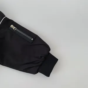 Detail of black jacket sleeve featuring a silver zippered pocket and ribbed cuff design
