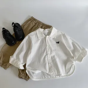 Flat lay of a white long-sleeve cotton shirt with cat embroidery and khaki casual pants