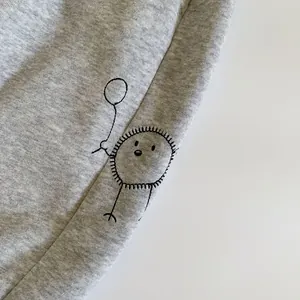 Détail du tissu en maille gris chiné avec personnage de dessin animé brodé et couture