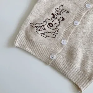 Close-up of beige knit cardigan fabric with reindeer embroidery and white buttons