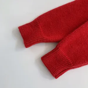 Dettaglio del polsino a coste di un maglione rosso lavorato a maglia con trama in lana
