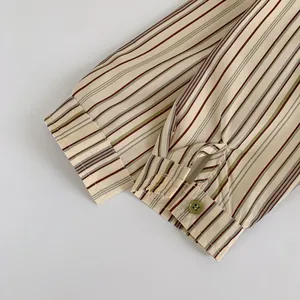 Détail du poignet d'une chemise rayée pour garçon avec bouton vert et coutures fines
