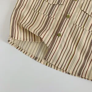 Détail macro du motif à rayures vintage et des boutons verts sur la chemise garçon