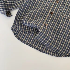 Détail d'une chemise en coton à carreaux bleu et blanc avec boutons bruns et ourlet arrondi