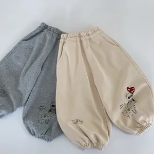 Détail de pantalons de jogging gris et beige pour enfants avec taille élastiquée et ours