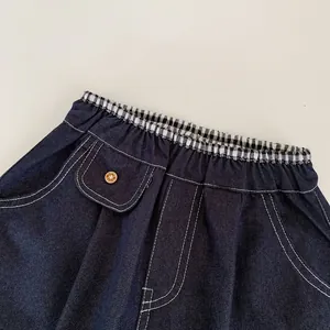 Détail du jean enfant avec taille élastique, bordure à carreaux et bouton en bois