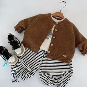 Flat lay of brown knit cardigan with wooden buttons and striped baby trousers