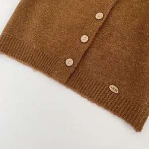 Detail of brown knit cardigan with wooden buttons and a small oval brand tag on hem