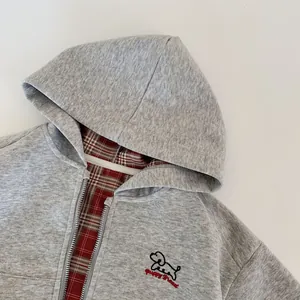 Detail of grey zip-up hoodie showing red tartan lining and small dog embroidery