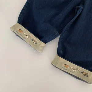 Détail de jean pour enfant avec ourlets retroussés, motifs d'animaux et broderies