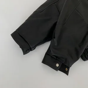 Detailed macro view of black leather jacket cuffs showing stitching and matte metal snaps