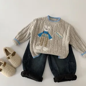 Détail d'un pull en maille beige avec broderie ours et bordures rayées bleues