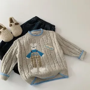 Détail du pull en maille torsadée grise avec écusson ours et finitions bleues contrastées