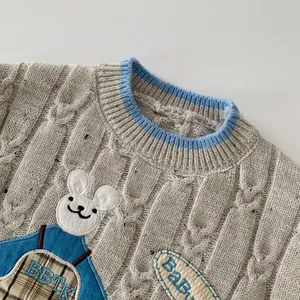 Détail de pull en maille torsadée grise pour enfant avec broderie lapin et col bleu côtelé