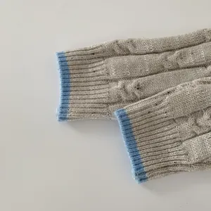 Détail de la maille torsadée et du bord-côte bleu clair sur une manche de pull gris hiver