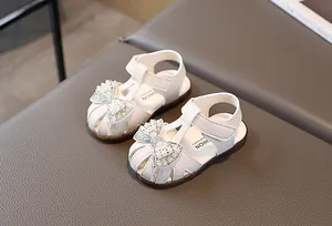 Close-up of white girls' sandals featuring pearl and rhinestone bow detail and T-strap