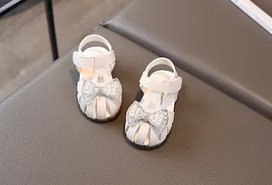 Close-up of white girls' sandals with rhinestone pearl bow and hollowed-out design
