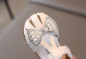 Close-up of cream white toddler sandal featuring a large pearl and rhinestone bow detail