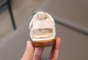 Detail view of toddler white sandals featuring a non-slip rubber sole and velcro closure