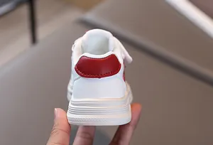 Close-up of white leather kids sneakers featuring red heel detail and non-slip rubber soles