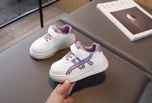 Detail view of children's white sneakers with purple trim and velcro straps on gray leather