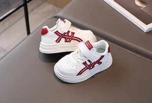 Detail view of white kids sneakers with red stripes and convenient velcro closure strap