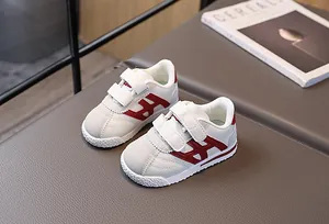 Detailed view of kids white sneakers with red H logo and double velcro closure strap