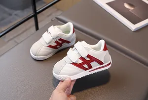 Close-up of children's white and red sneakers featuring velcro straps and textured leather