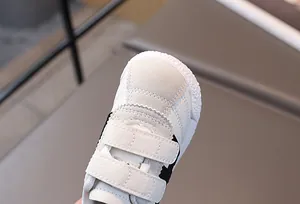 Detail of white kids sneakers featuring dual velcro straps and premium stitched leather