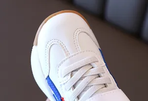 Detail of kids white sneaker showing leather texture, blue-red stripes and gum sole