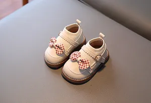 Détail de chaussures bébé fille en cuir crème avec un nœud en damier rouge et blanc