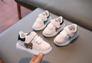 Three pairs of white leather kids sneakers featuring plush bear patches and velcro straps