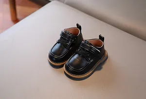 Dettaglio scarpe neonato in pelle nera con chiusura a strappo e cuciture marroni