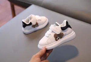 Detail of white toddler sneaker with velcro strap and a cute brown plush bear patch
