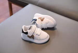Close-up of toddler white sneakers featuring a cute plush bear and velcro closure