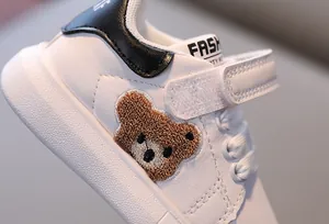 Detail of children white sneaker featuring brown plush bear embroidery and velcro strap