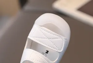 Close-up of baby beach sandals featuring a white leather upper and hook-and-loop strap