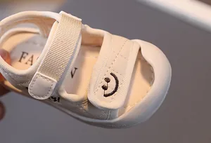 Dettaglio di sandali per neonati in pelle crema trapuntata con ricamo a forma di sorriso