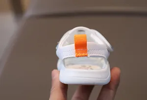 Detail of baby sandal heel showing the orange pull tab and soft white leather material