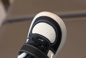 Détail de baskets bébé montrant coutures blanches, perforations et sangle velcro