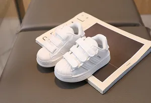 Detail of white kids sneakers featuring shell toe design and triple hook-loop straps
