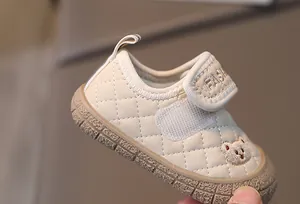 Detail of baby walking shoes with quilted fabric, bear embroidery, and non-slip rubber sole