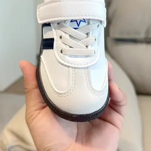 Detail of white leather kids sneakers featuring black stripes and velcro strap closure